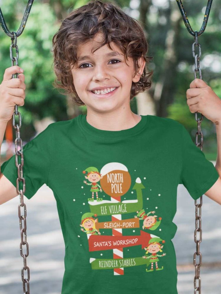 happy boy in a green tshirt with elves on a north pole signpost