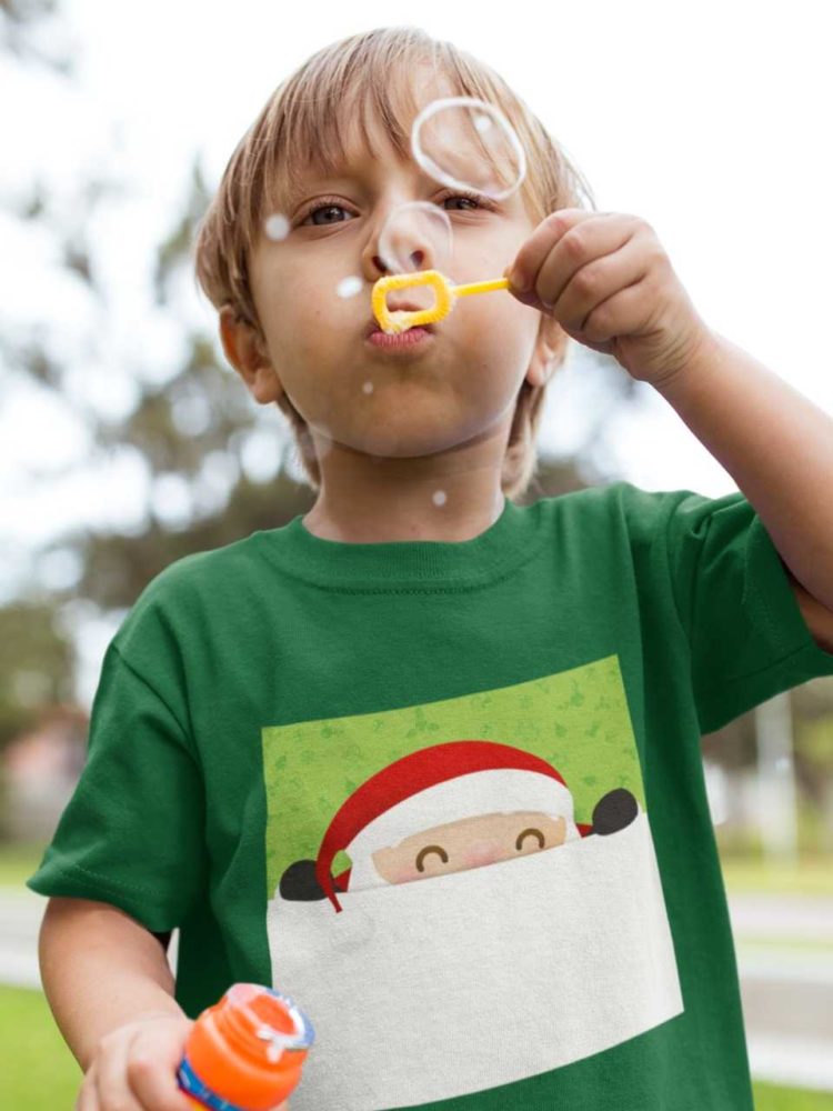 little boy blowing bubbles in a green tshirt with Santa peeping out